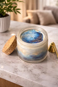 Sea Salt & Rosemary Candle in a decorative jar with blue and gold hues on a marble surface.