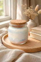 Sea Salt & Rosemary Candle in glass jar with cork lid, displayed on wooden tray near books and dried flowers.