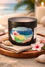 Seaside Blossom Candle in an elegant black jar with floral design on a wooden tray surrounded by seashells.