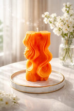 Decorative Sparkling Blossom Candles - vibrant orange candle with wavy design on a marble tray, surrounded by flowers.