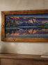 Sunset over Still Waters Diamond Painting displayed in a wooden frame above a console table with decor.