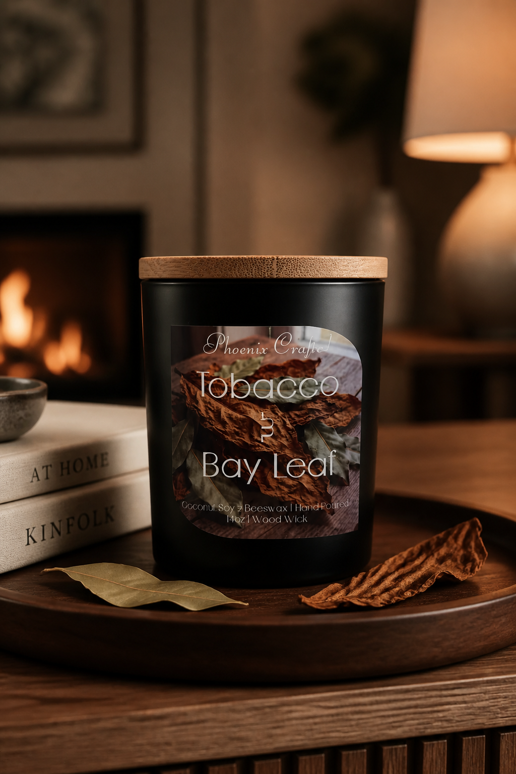 Matte black jar candle with wooden lid labeled 'Tobacco & Bay Leaf' sits on a wooden tray with bay and dried tobacco leaves.