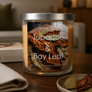 Jar candle with lid and label on a table beside a folded beige napkin and small dish of bay leaves, blurred lamp behind.