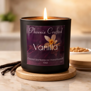 Matte black cylindrical candle jar with purple 'Phoenix Crafted Vanilla' label, lit single wick.