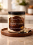 Vanilla Harvest Candle in a glass container on a wooden tray with vanilla pods and flowers.