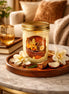 Vanilla Orchid & Sandalwood Candle in a jar surrounded by flowers and wooden elements on a marble table.