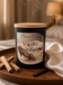 Black matte jar candle with pale lid on a round tray beside palo santo sticks, a dark pod, and a cream cloth.