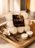 Vanilla Tealights in a pack with vanilla pods and a flower on a wooden tray, showcasing cozy candlelight.