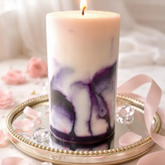 Viva La Juicy Artisan Pillar candle with marbled purple and white design, lit and placed on a decorative mirror.