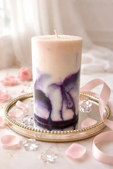 Cylindrical pillar candle with cream top and purple marbled lower half, single wick, on a round mirrored tray with beaded rim, pink petals and ribbon