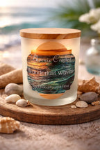 Wanderlust Waves Candle with wooden lid, displayed with seashells and stones on a coastal backdrop.