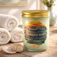 Clear mason jar candle with gold screw lid and pale green wax, 'Wanderlust Waves' label with ocean sunset art.