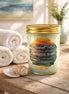 Clear mason jar candle with gold screw lid and pale green wax, 'Wanderlust Waves' label with ocean sunset art.