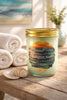 Clear mason jar candle with gold screw lid and pale green wax, 'Wanderlust Waves' label with ocean sunset art.