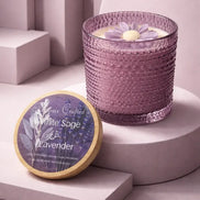 Lavender-hued textured glass candle with cream wax and a purple flower topper.