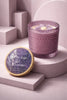 Lavender-hued textured glass candle with cream wax and a purple flower topper.