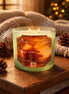 Pale green frosted glass jar candle with two lit wicks and orange label reading 'Phoenix Crafted — Winter Solstice Glow'.