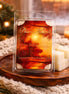Clear clamshell of white segmented wax melts with a warm orange label, stacked on a round wooden tray with a knitted blanket and a candle blurred.