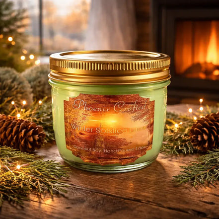 Green wax candle in a clear glass jar with a gold screw lid, label showing 'Phoenix Crafted' and 'Winter Solstice Glow'.