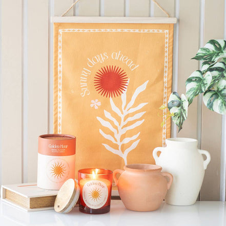 Orange wall hanging reading 'Sunny days ahead' above an amber candle labeled 'Golden Hour', matching box.