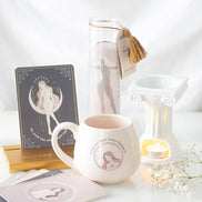 White Greek-column wax warmer with pale pink mug reading 'Embrace Your Inner Goddess', tall 'ATHENA' candle with gold tassel.