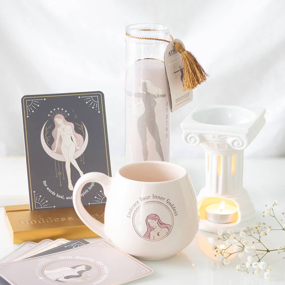 White Greek-column wax warmer with pale pink mug reading 'Embrace Your Inner Goddess', tall 'ATHENA' candle with gold tassel.