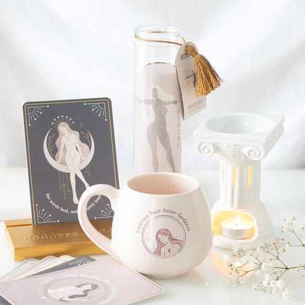 White Greek-column wax warmer with pale pink mug reading 'Embrace Your Inner Goddess', tall 'ATHENA' candle with gold tassel.