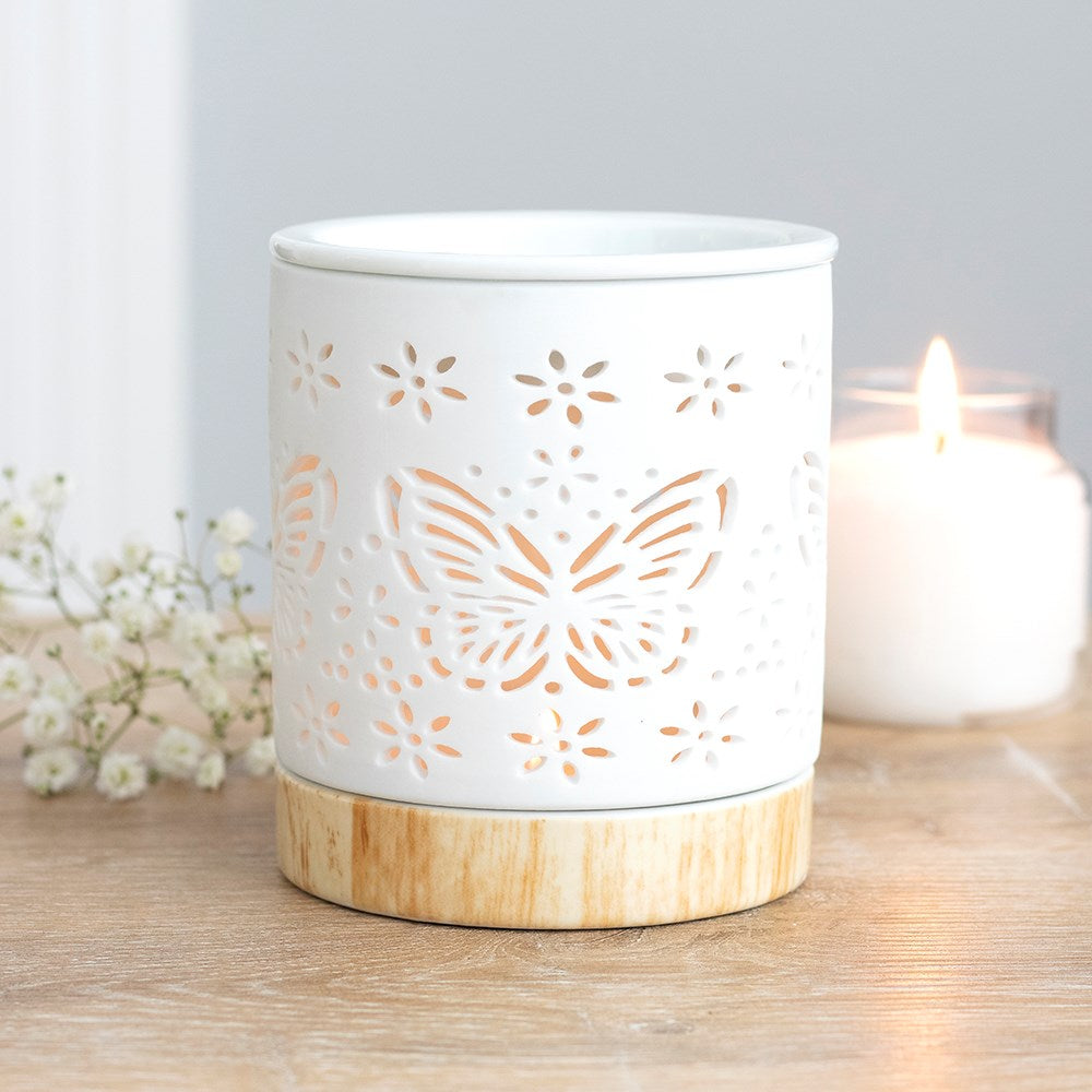 Matte ceramic butterfly oil burner with cut-out design illuminating a tealight candle.