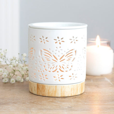 Matte ceramic butterfly oil burner with cut-out design illuminating a tealight candle.