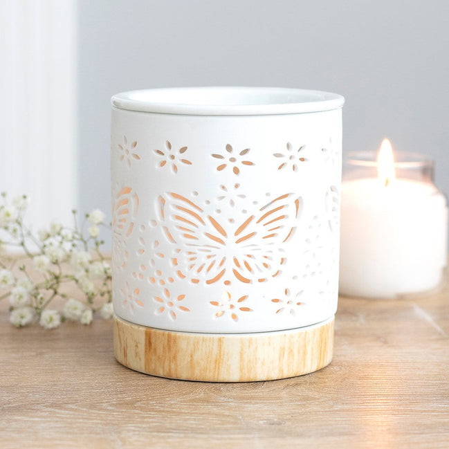 Matte ceramic butterfly oil burner with cut-out design illuminating a tealight candle.