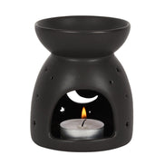 Matte black ceramic wax warmer with top bowl, arched front opening showing a lit tealight in a silver cup and crescent moon and star cutouts.