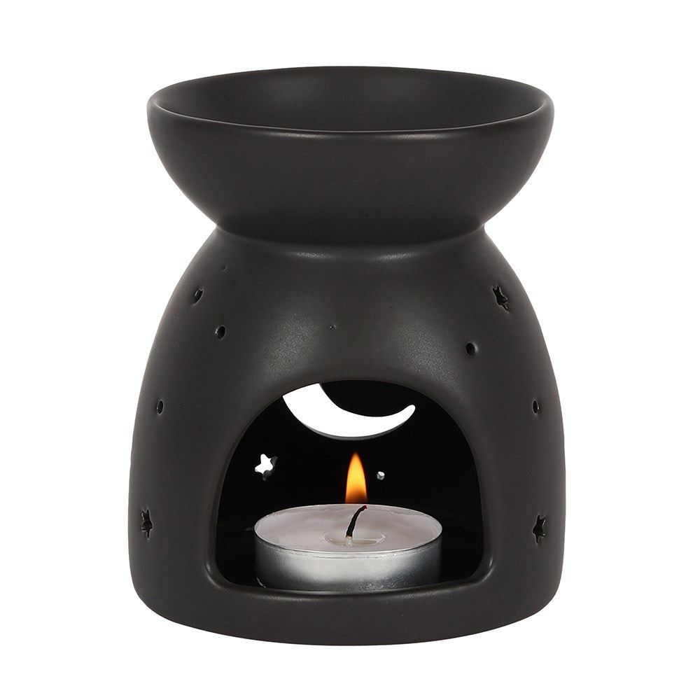 Matte black ceramic wax warmer with top bowl, arched front opening showing a lit tealight in a silver cup and crescent moon and star cutouts.