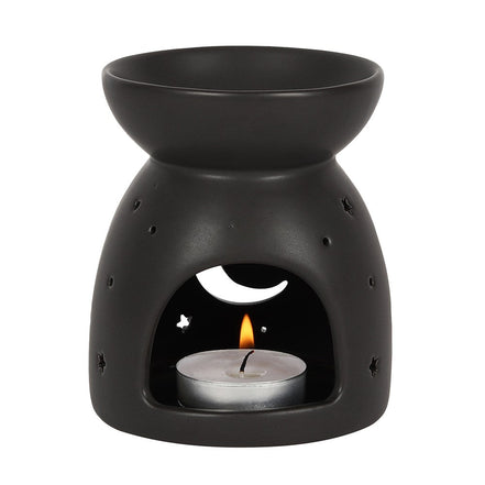 Matte black ceramic wax warmer with top bowl, arched front opening showing a lit tealight in a silver cup and crescent moon and star cutouts.