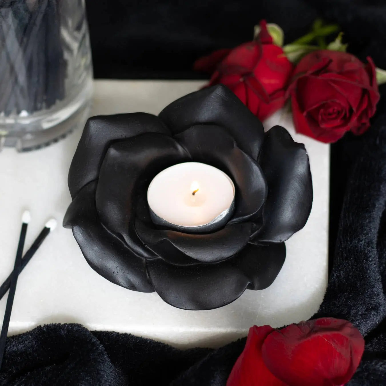 Black rose tealight candle holder with a lit tealight, surrounded by red roses and black decor.