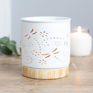 White cylindrical ceramic wax warmer with dragonfly and floral cutouts on a light wood-effect round base.