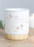 White cylindrical ceramic wax warmer with dragonfly and floral cutouts on a light wood-effect round base.