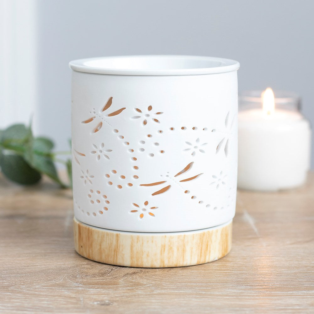 White cylindrical ceramic wax warmer with dragonfly and floral cutouts on a light wood-effect round base.