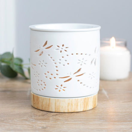 White cylindrical ceramic wax warmer with dragonfly and floral cutouts on a light wood-effect round base.