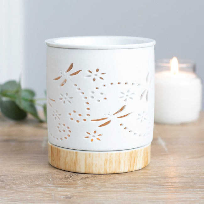 White cylindrical ceramic wax warmer with dragonfly and floral cutouts on a light wood-effect round base.