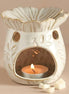 Cream ceramic wax warmer with scalloped bowl, gold trim, leaf pattern, round vents and arched front revealing a lit tealight in a metal cup and wax.