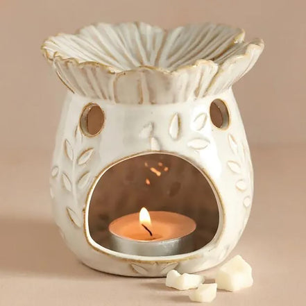 Cream ceramic wax warmer with scalloped bowl, gold trim, leaf pattern, round vents and arched front revealing a lit tealight in a metal cup and wax.