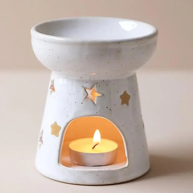 Starry wax melt ceramic warmer with star cut-outs, featuring a tealight candle in the base, creating a warm ambiance.
