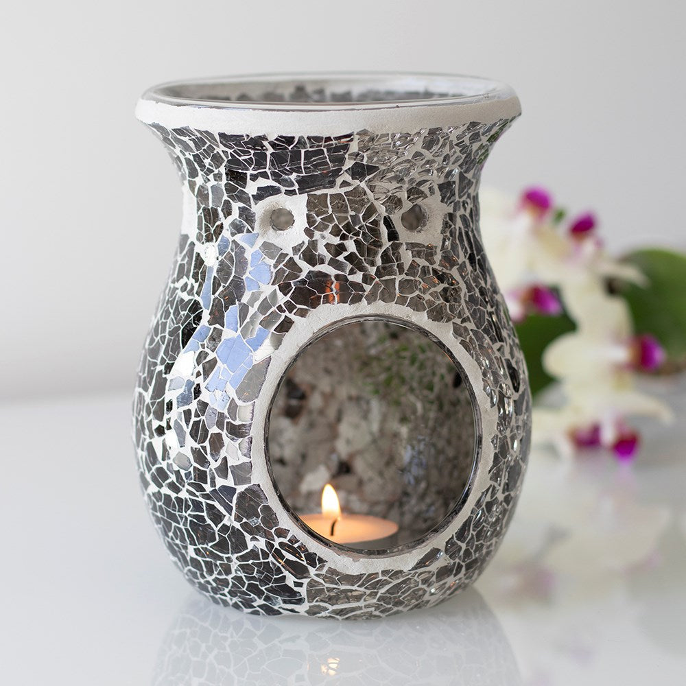 Gunmetal grey crackle mosaic oil burner with round front opening, lit tealight inside, silver rim and blurred orchid background