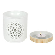 White ceramic cylindrical oil burner with circular mandala cutout; shallow round dish with light wood rim holding a lit tealight