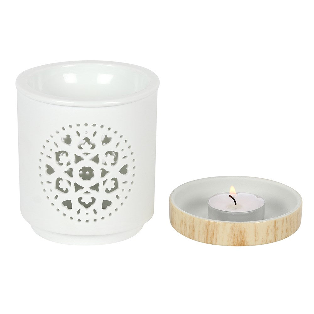 White ceramic cylindrical oil burner with circular mandala cutout; shallow round dish with light wood rim holding a lit tealight