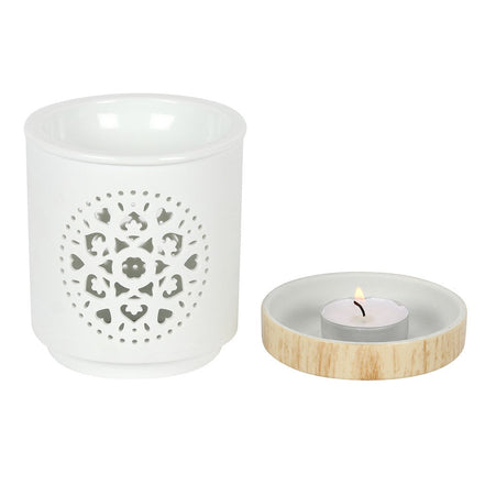 White ceramic cylindrical oil burner with circular mandala cutout; shallow round dish with light wood rim holding a lit tealight
