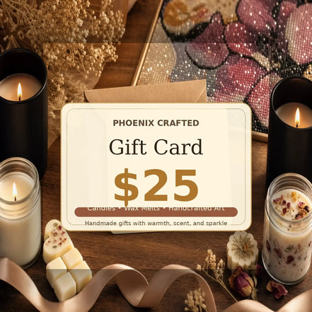 Beige and gold $25 Phoenix Crafted gift card in a brown envelope on a wood table, flanked by lit black and glass candles, wax melts.