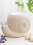 Beige stone snail-shaped wax warmer with carved spiral shell and smiling face, shallow bowl top.