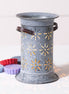 Weathered gray cylindrical metal wax warmer with starburst cutouts and wooden side handles, casting star-shaped shadows beside colorful wax melts.