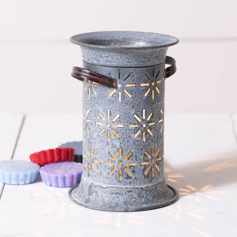 Weathered gray cylindrical metal wax warmer with starburst cutouts and wooden side handles, casting star-shaped shadows beside colorful wax melts.